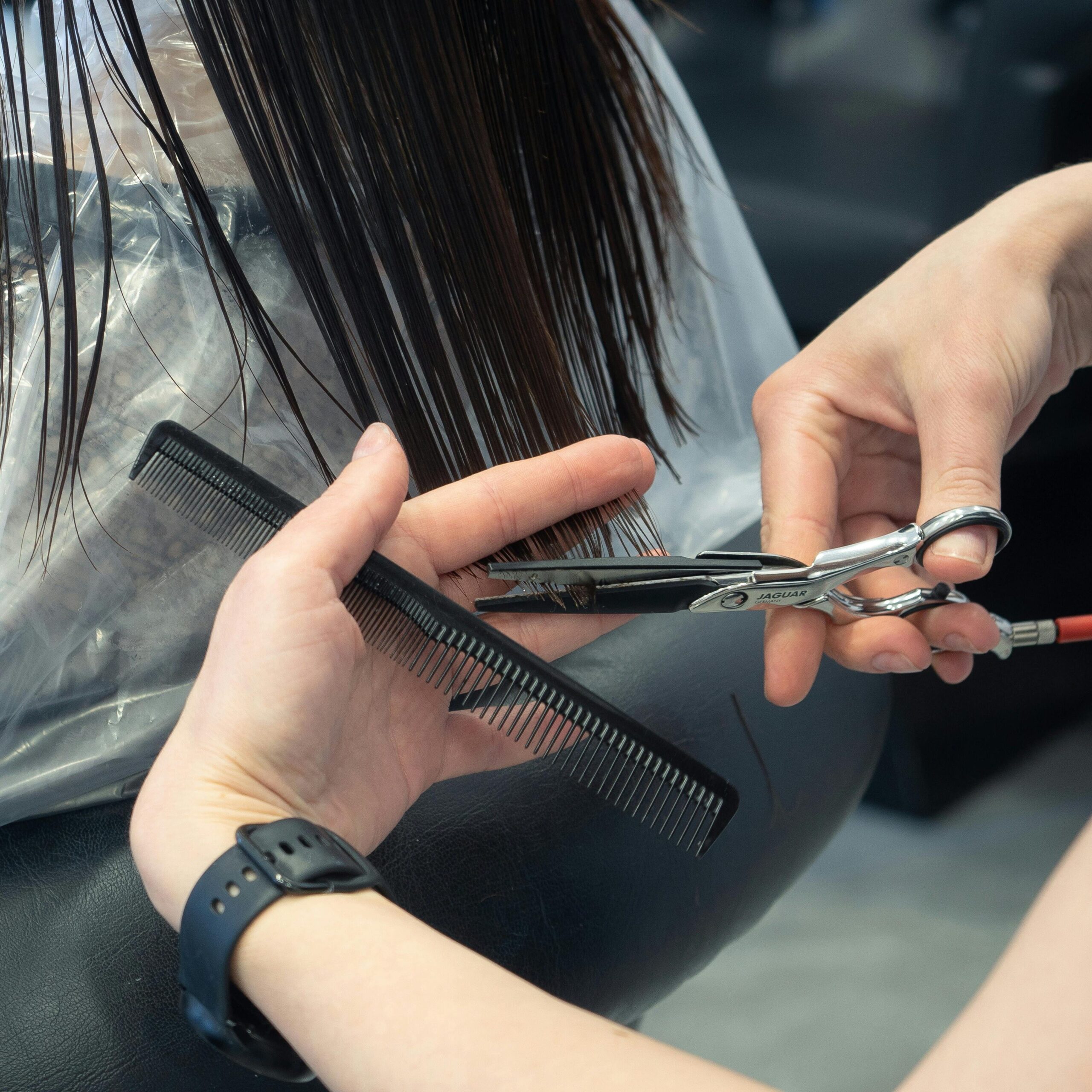Close-up of a stylist cutting hair with scissors and comb during a salon haircut.