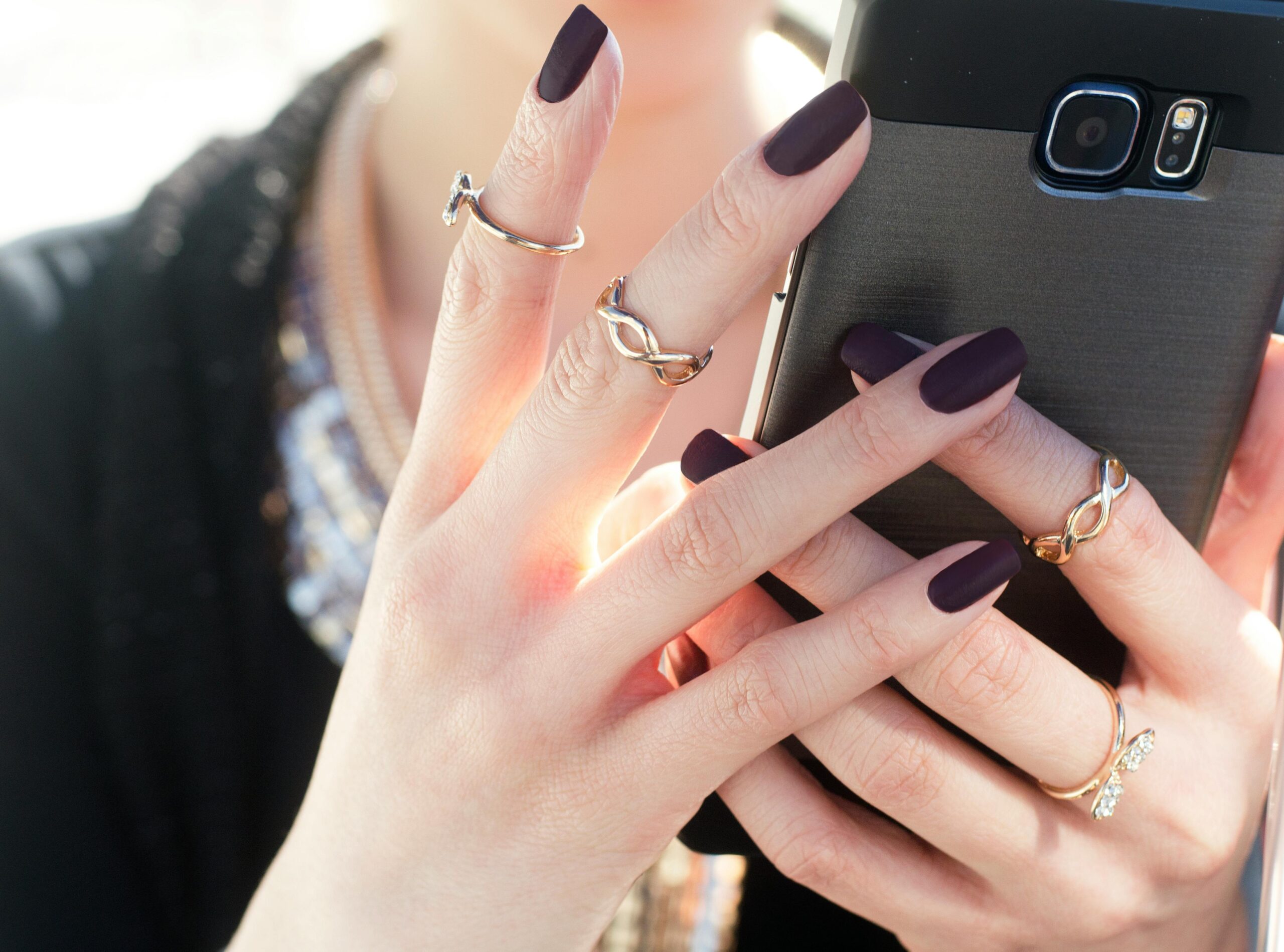 Services Close-up of a woman with manicured nails and rings holding a smartphone, showcasing fashion elegance.