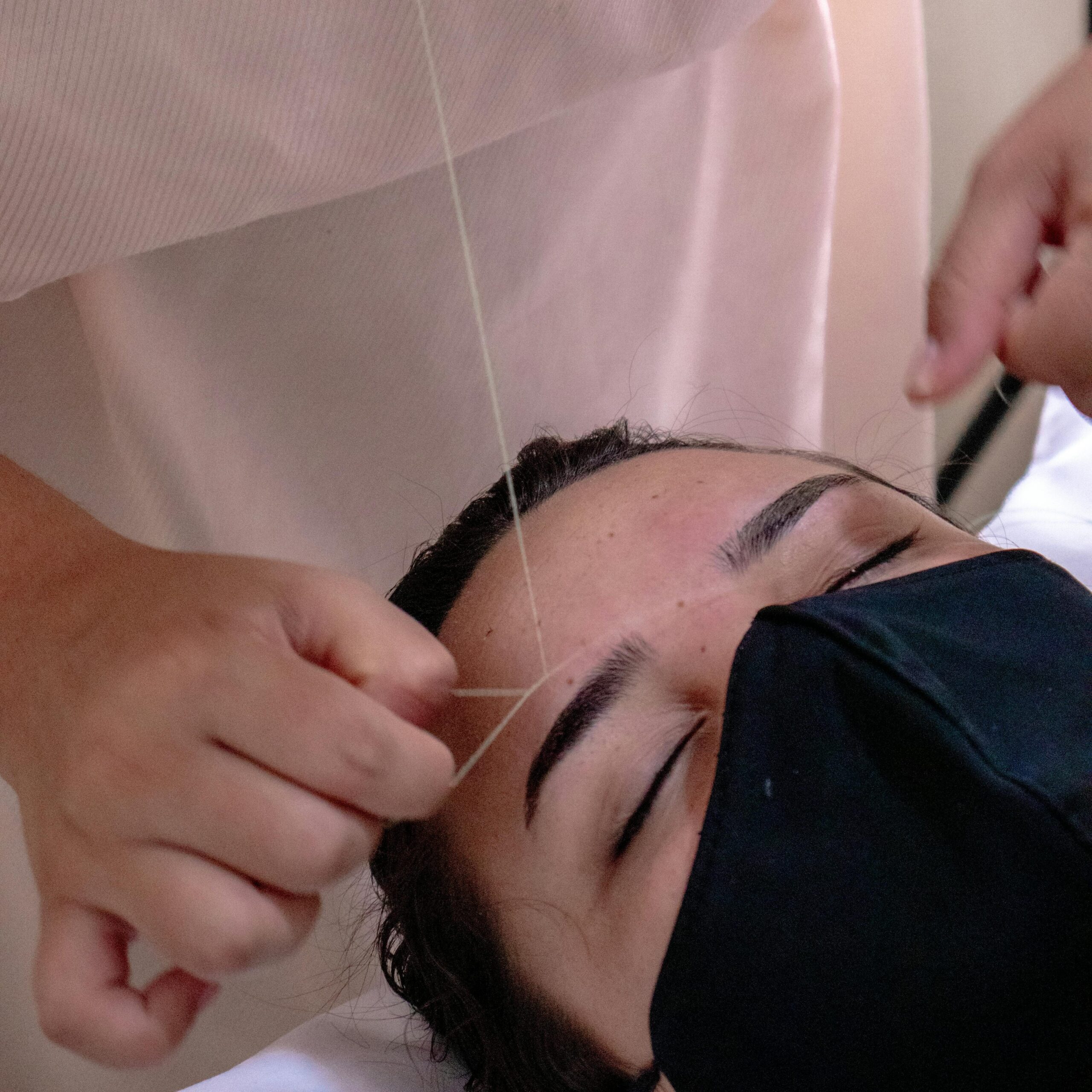 Close-up of eyebrow threading procedure in a salon, highlighting beauty and precision.
