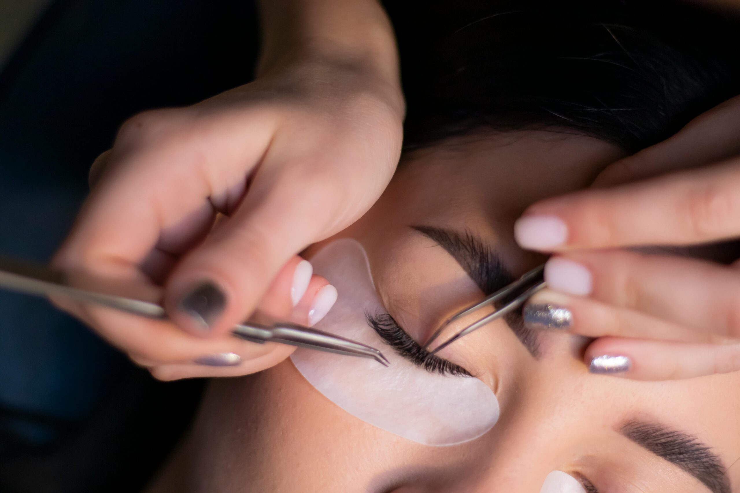 Services Detailed view of a beautician applying eyelash extensions to a woman